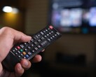 Hand holding a remote control with a blurred TV in the background