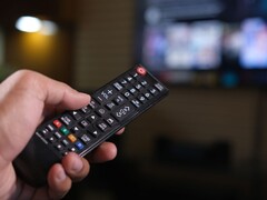 Hand holding a remote control with a blurred TV in the background
