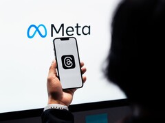 A hand holds a smartphone in front of a large Meta logo