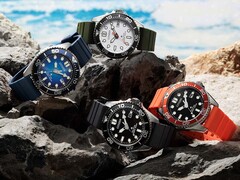 Four Citizen Promaster Marine dive watches in white, black, blue, and orange colorways displayed on rocks by the seaside.
