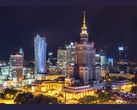Nighttime cityscape of Warsaw featuring the illuminated Palace of Culture and Science surrounded by modern skyscrapers and office buildings.