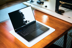 An open matte black Razer Blade 16 gaming laptop sitting on a white desk mat over a warm wooden table, displaying a vivid black-and-white wallpaper.