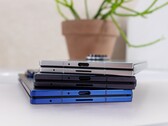 Stack of foldable smartphones representing the concept of the upcoming Apple iPhone Fold, placed on a white table with a potted plant in the background (Image source: Notebookcheck)