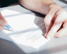 A hand signs a document with a blue ballpoint pen