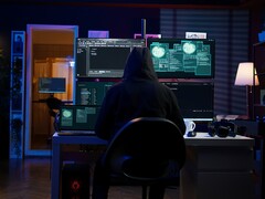 Hooded figure at a multi-screen setup running a cyberattack.
