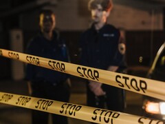 Two police officers standing at night behind a yellow tape that reads Stop
