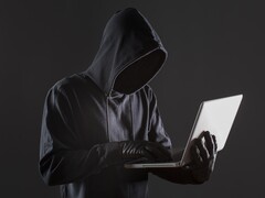A hooded hacker operating a laptop against a dark background.