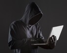 A hooded hacker operating a laptop against a dark background.