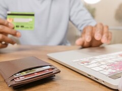 Person holding a bank card in front of a laptop, with a wallet on the desk