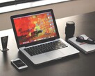 MacBook Pro on a dark desk next to a smartphone, glasses, and notebook