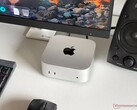 Apple M6 Mac mini on a desk in a gaming setup with a monitor, keyboard, mouse and speaker.