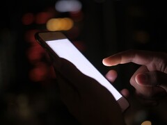 Hand holding a smartphone with a glowing screen in the dark
