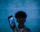 Floating smartphone with code on its screen in front of a blue background, with a blurred person behind it