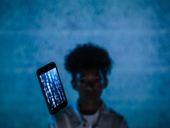 Floating smartphone with code on its screen in front of a blue background, with a blurred person behind it
