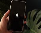 A hand holds an iPhone, the Apple logo and a progress bar are lit on the screen.