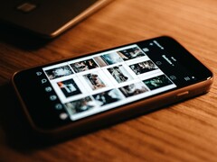 A smartphone lying on a wooden desk, its display showing a grid of photos